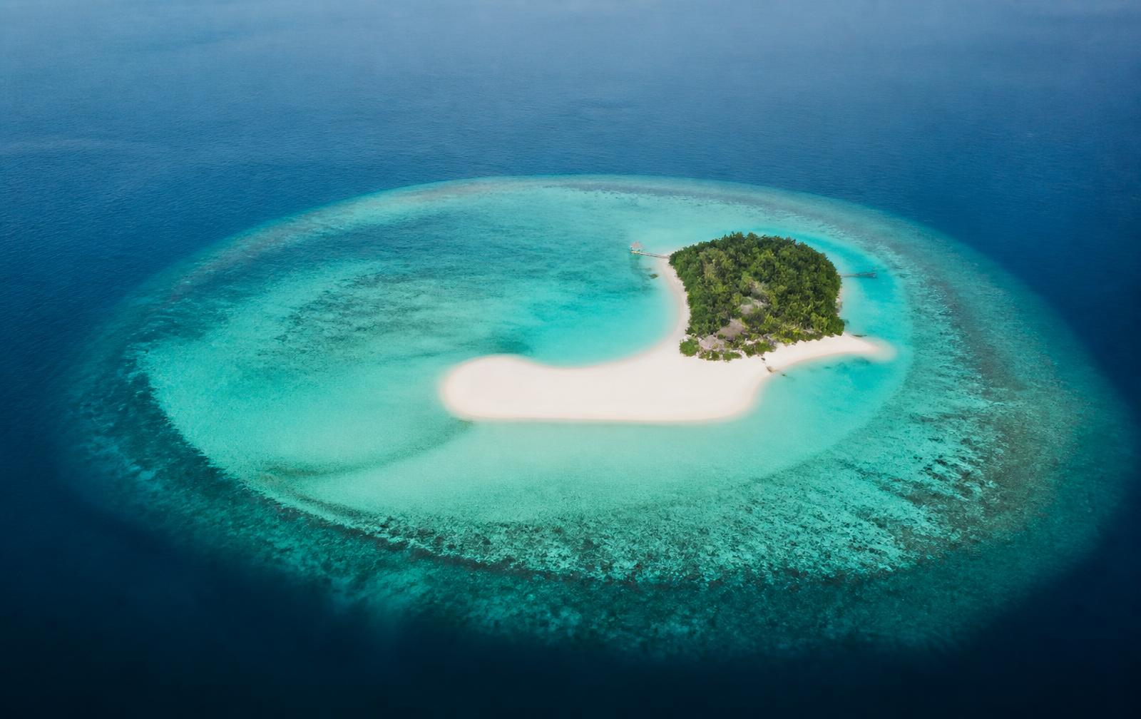 Aerial view of a small Maldivian island ringed by a turquoise lagoon and sandbank